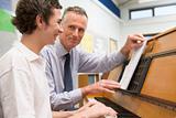 Teacher with schoolboy playing piano in music class