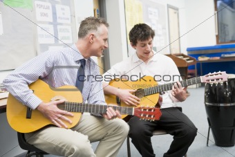 Schoolboy and teacher playing guitar in music class