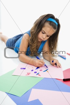 Hispanic girl coloring on floor.