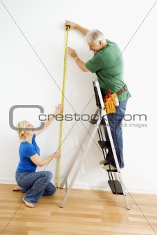 Man and woman measuring wall.