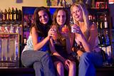 Three young women sitting on a bar counter, enjoying cocktails