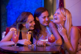 Three young women sitting at a table and laughing in a nightclub