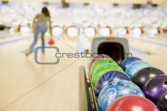 Bowling ball machine with woman bowling in the background