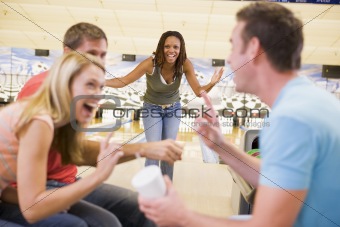 Four young adults laughing and gesturing in a bowling alley