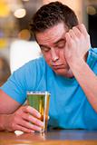 Young man with beer falling asleep at bar