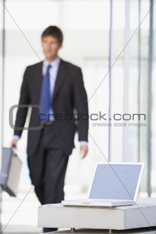 Laptop sitting in office lobby with businessman walking in