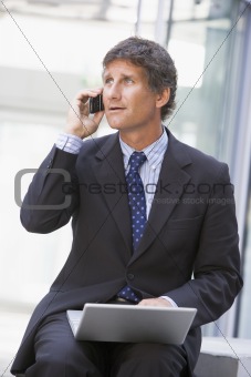 Businessman sitting in office lobby with laptop using cellular p
