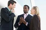 Three businesspeople standing outdoors by building talking and s