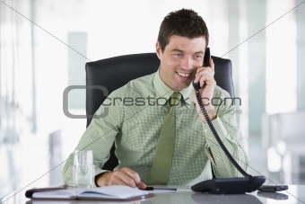 Businessman sitting in office with personal organizer on telepho