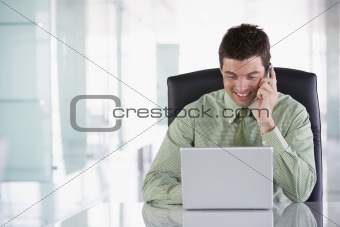 Businessman sitting in office using cellular phone and laptop