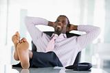 Businessman sitting in office with feet on desk relaxing and smi