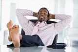 Businessman sitting in office with feet on desk relaxing and smi