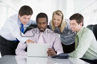 Four businesspeople in a boardroom pointing at laptop and smilin