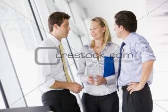 Three businesspeople standing in corridor talking and smiling