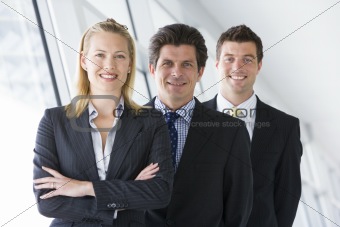 Three businesspeople standing in corridor smiling