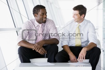 Two businessmen sitting in office lobby talking and smiling