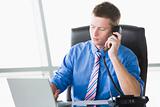 Businessman sitting in office with laptop on telephone