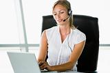 Businesswoman sitting in office wearing headset using laptop