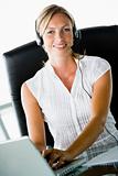 Businesswoman sitting in office wearing headset using laptop and