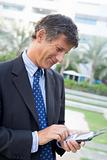 Businessman outdoors using personal digital assistant smiling