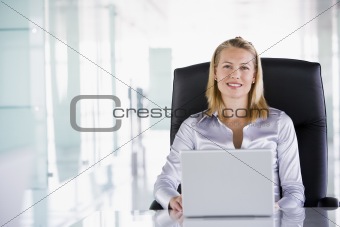 Businesswoman sitting in office with laptop smiling