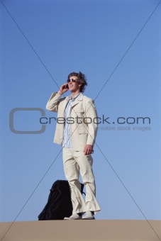 Man outdoors with suitcase using cellular phone