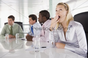 Four businesspeople in boardroom with one businesswoman yawning