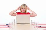 Businesswoman sitting in boardroom with laptop looking frustrate
