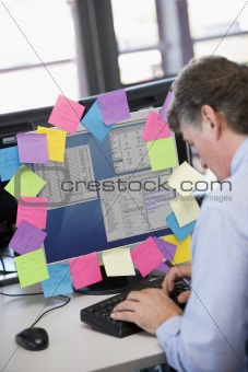 Businessman in office typing at computer with notes on it
