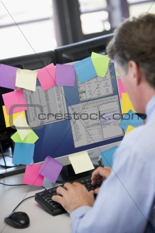 Businessman in office typing at computer with notes on it