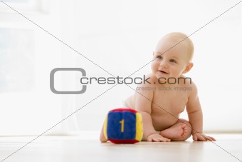 Baby sitting indoors with block smiling
