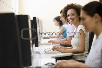Four people in computer room typing and smiling