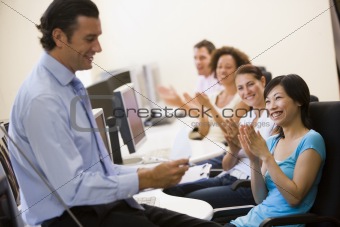 Man with clipboard giving lecture in applauding computer class