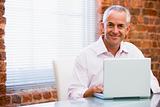 Businessman sitting in office on laptop smiling