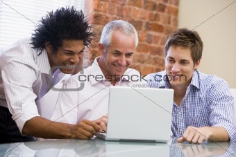 Three businessmen sitting in office with laptop smiling