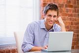 Businessman sitting in office with laptop smiling