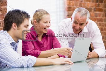 Three businesspeople in office with laptop pointing and laughing