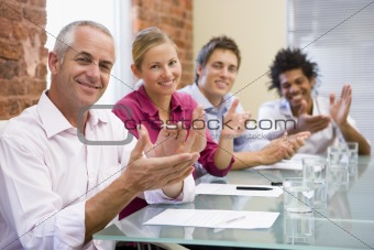 Four businesspeople in boardroom applauding and smiling