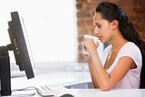 Businesswoman in office drinking coffee and looking at computer
