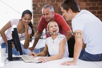 Four businesspeople in office space with computer smiling