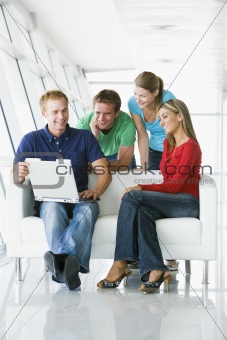 Four people in lobby looking at laptop smiling