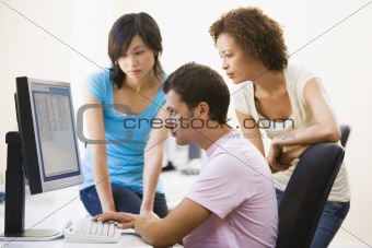Three people sitting in computer room looking at monitor