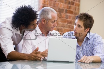 Three businessmen in office with laptop talking