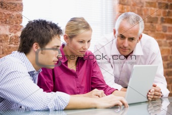 Three businesspeople in office looking at laptop