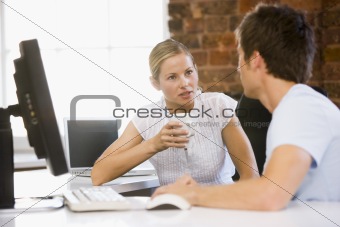 Two businesspeople in office drinking coffee and talking