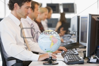 Five businesspeople in office space with a desk globe in foregro