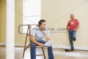 Two men with ladder in empty space one holding paper smiling