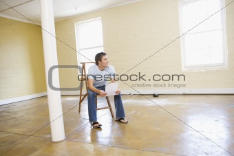 Man sitting on ladder in empty space holding paper smiling