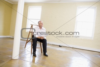 Man sitting on ladder in empty space holding paper smiling