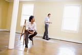 Man sitting on ladder in empty space with another man holding pa
